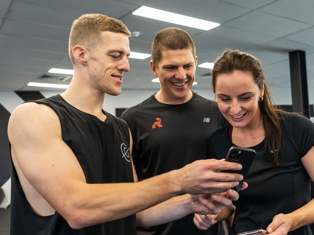 Three people looking at a training program on a phone in the gym